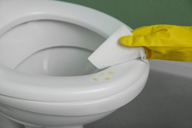 Photo of Woman wiping urine drops from toilet seat in restroom, closeup