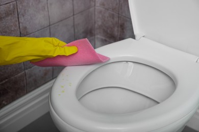 Photo of Woman wiping urine drops from toilet seat in restroom, closeup