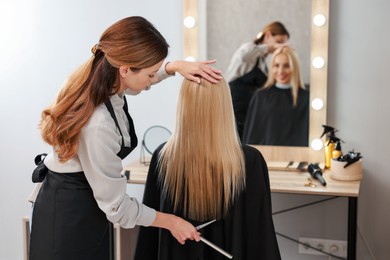 Photo of Professional hairdresser combing woman's hair in salon