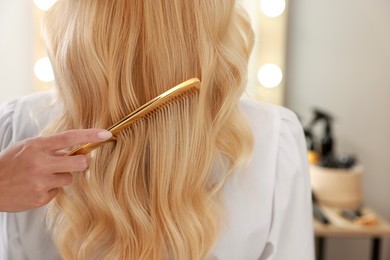 Photo of Professional hairdresser combing woman's hair in salon, closeup