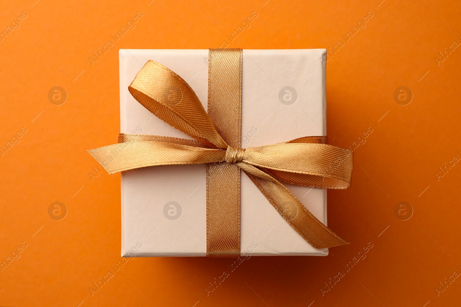 Photo of Beautiful gift box with golden bow on orange background, top view