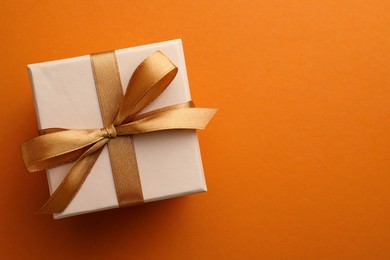 Photo of Beautiful gift box with golden bow on orange background, top view. Space for text