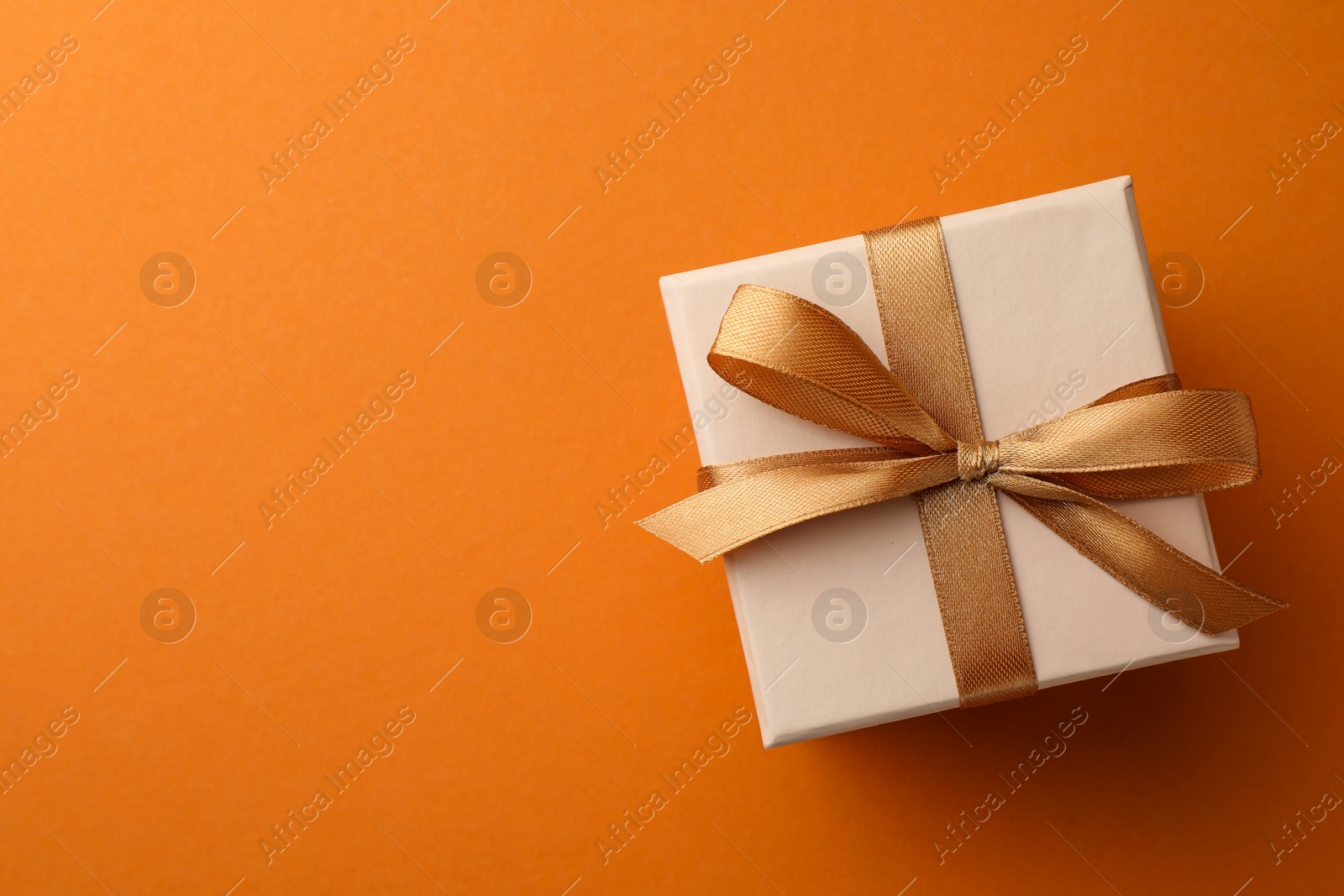 Photo of Beautiful gift box with golden bow on orange background, top view. Space for text