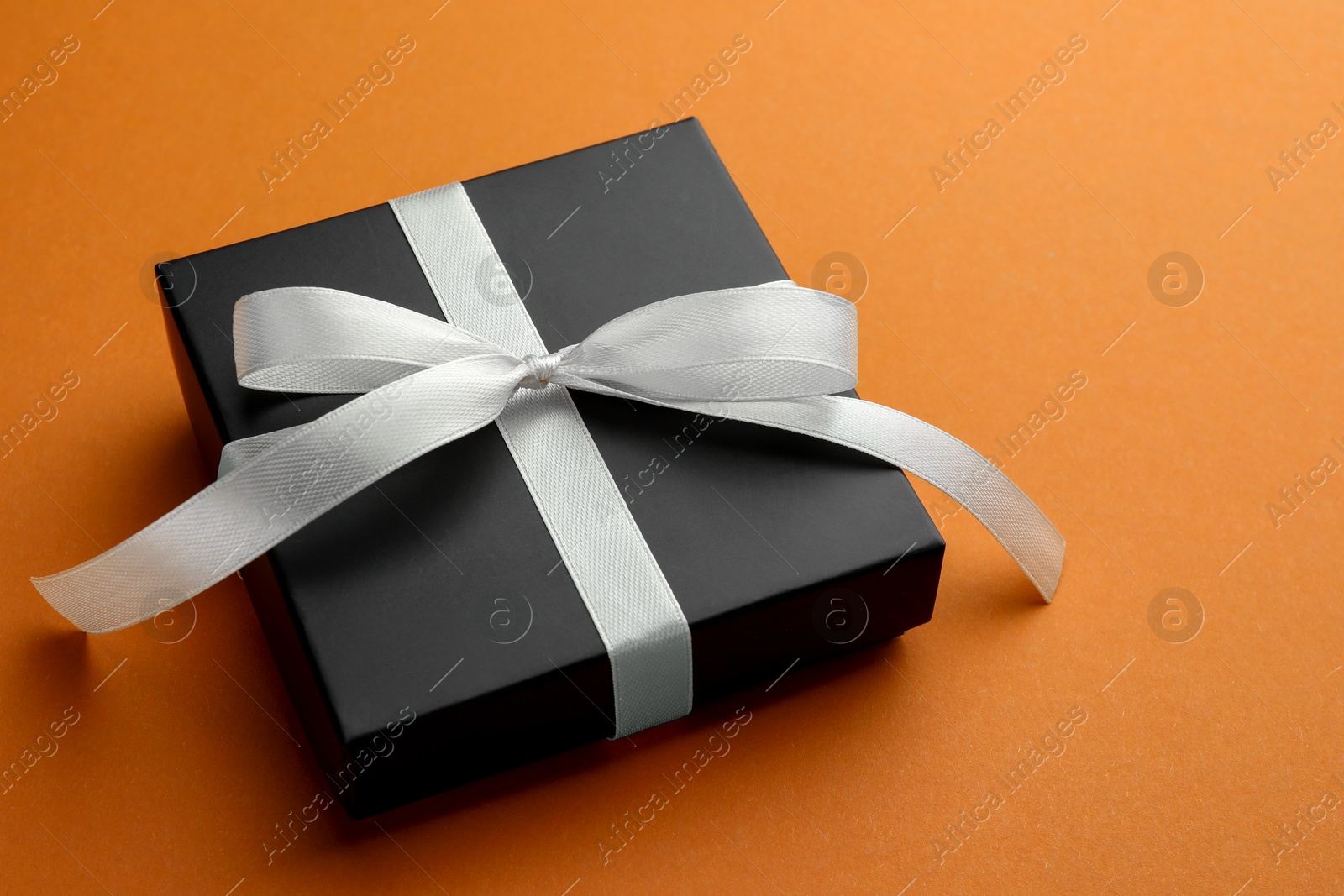 Photo of Beautiful gift box with bow on orange background, closeup