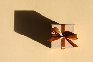 Photo of Beautiful gift box with golden bow casting shadow of house on beige background, top view. Space for text