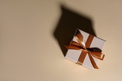 Photo of Beautiful gift box with golden bow casting shadow of house on beige background, top view. Space for text