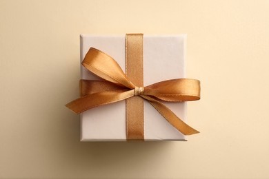 Beautiful gift box with golden bow on beige background, top view