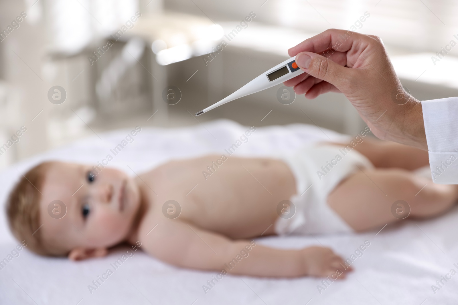 Photo of Pediatrician examining little child with thermometer in clinic, selective focus. Checking baby's health