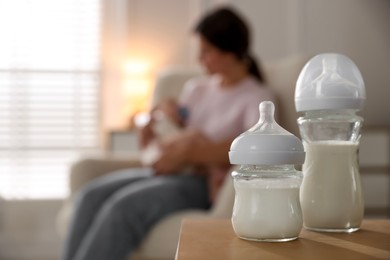 Photo of Mother holding her little baby indoors, focus on bottles with milk