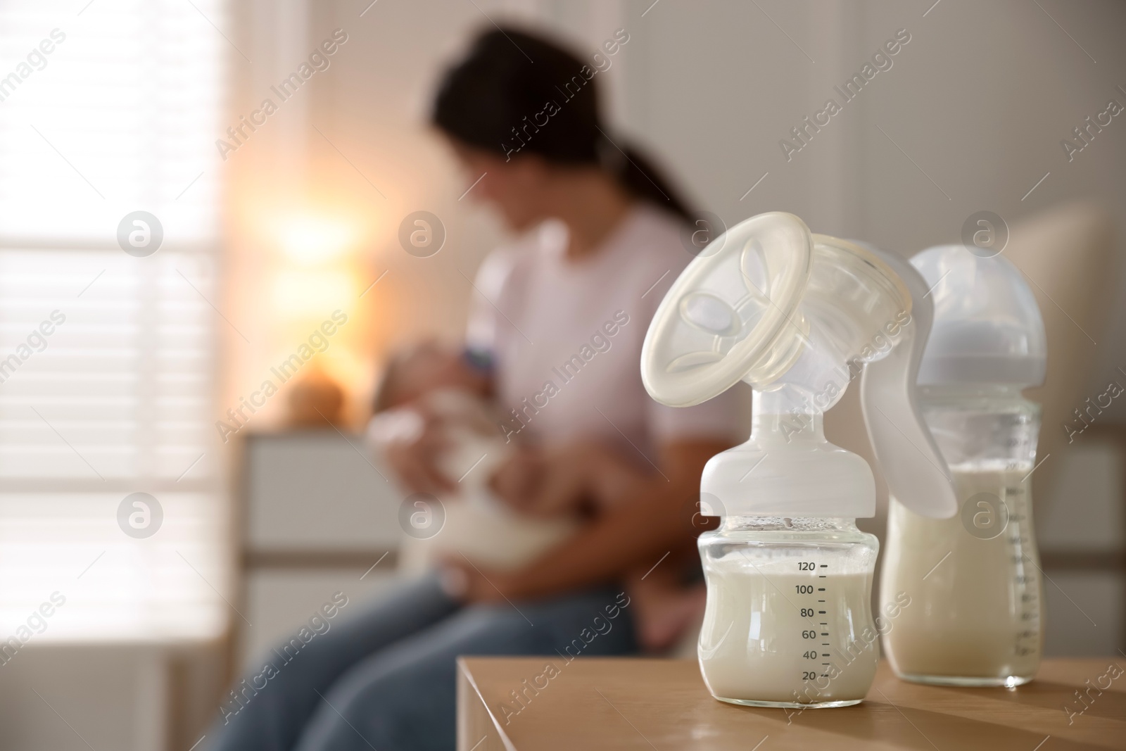 Photo of Mother holding her little baby indoors, focus on breast pump with milk and bottle