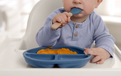 Photo of Cute little baby eating healthy food in high chair indoors, closeup