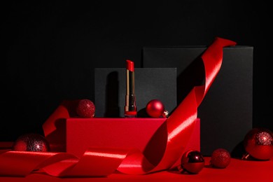 Photo of Christmas present. Red lipstick, boxes and festive decor against black background