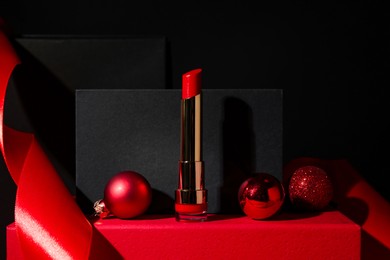 Photo of Christmas present. Red lipstick, boxes and festive decor against black background. Space for text