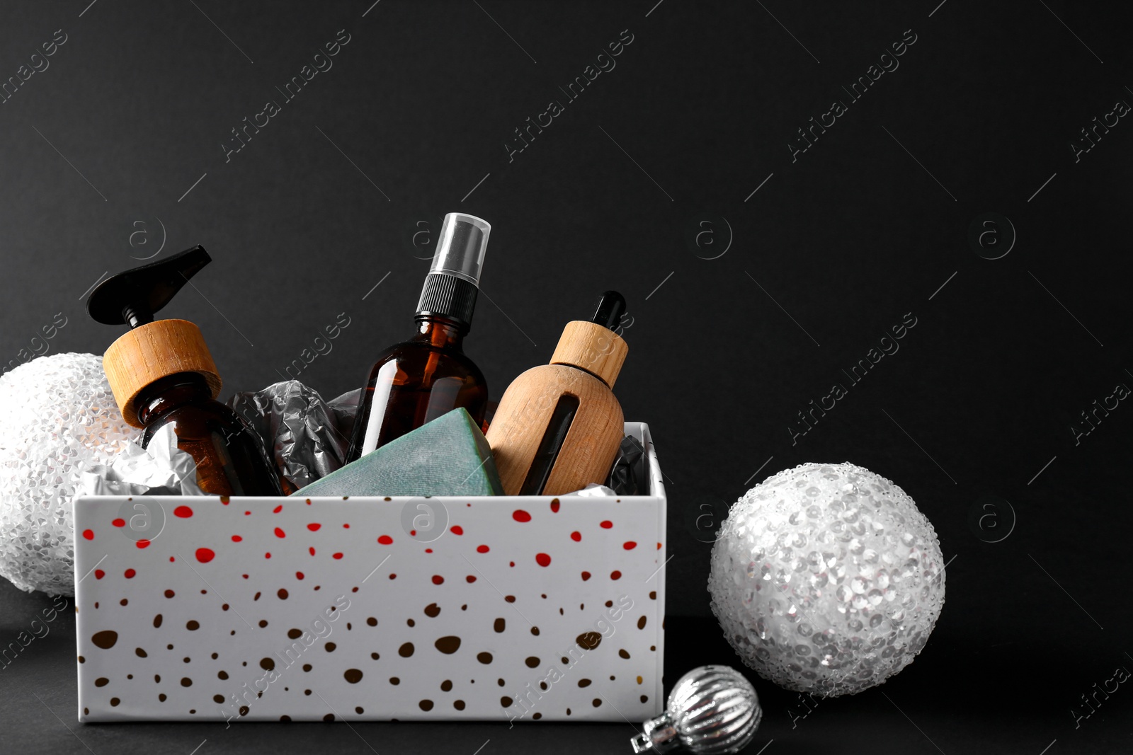 Photo of Cosmetic products in box as Christmas gift and festive balls on black background. Space for text