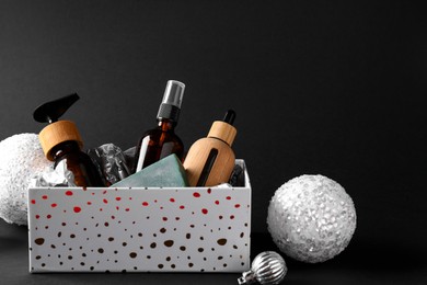 Cosmetic products in box as Christmas gift and festive balls on black background. Space for text