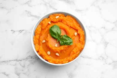 Photo of Tasty mashed sweet potato with basil and seeds in bowl on white marble table, top view