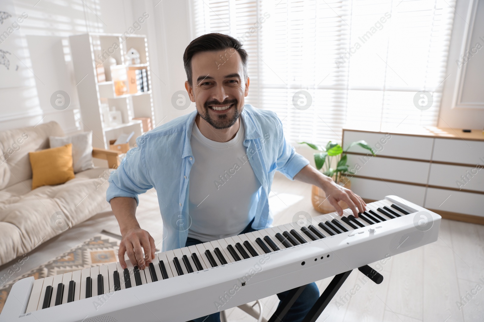 Photo of Smiling man playing synthesizer at home. Electronic musical instrument