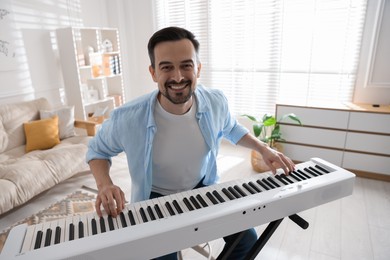 Smiling man playing synthesizer at home. Electronic musical instrument