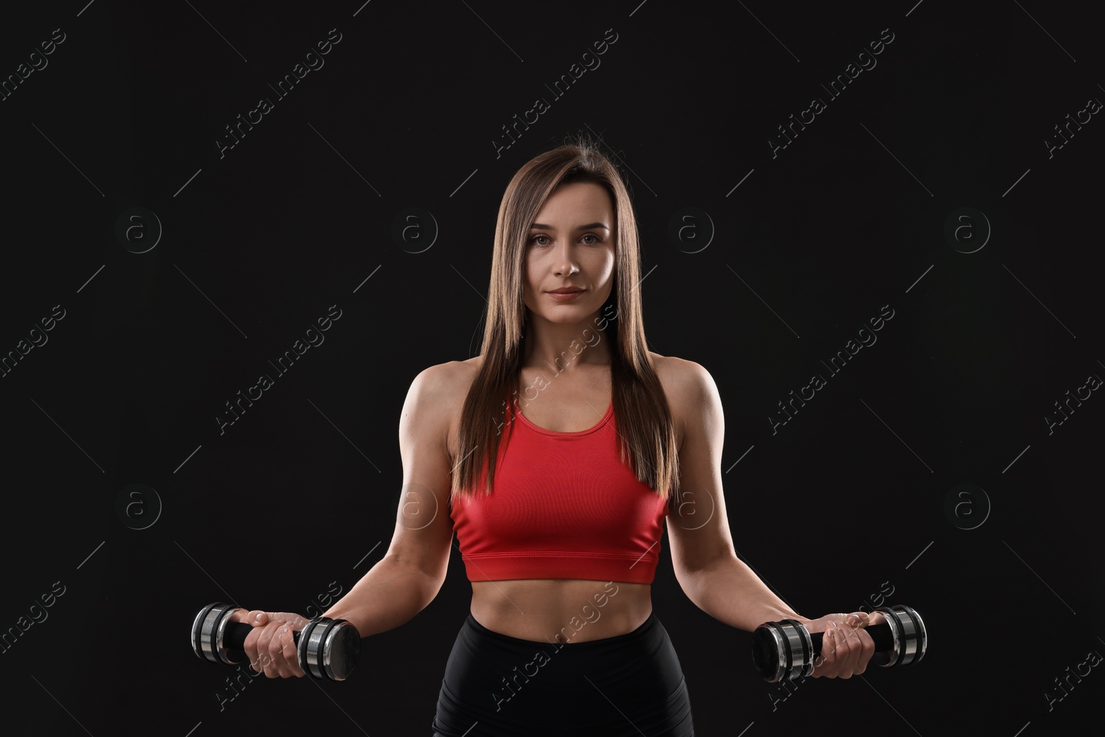 Photo of Woman in gym clothes exercising with dumbbells on black background