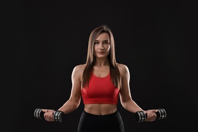 Woman in gym clothes exercising with dumbbells on black background