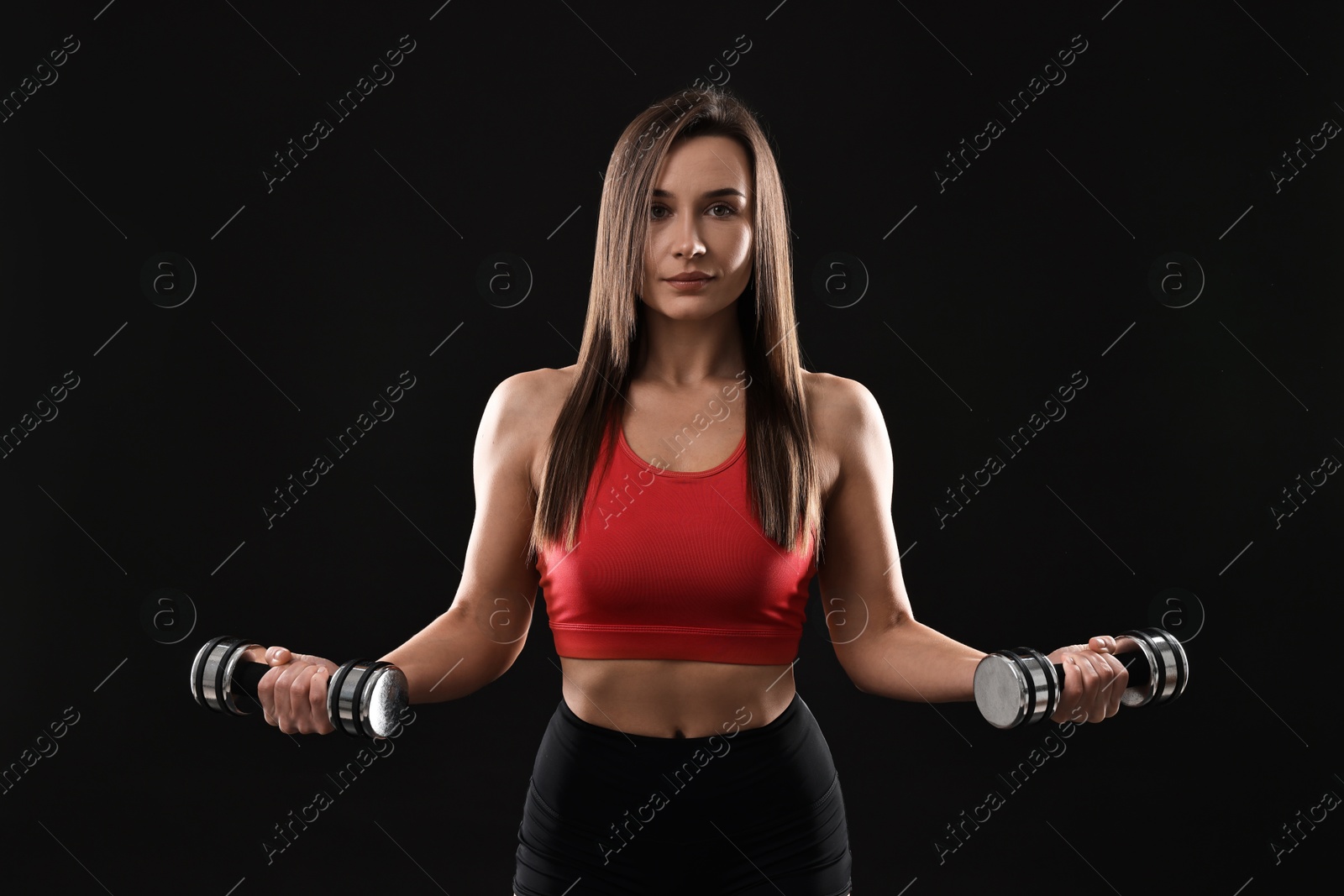 Photo of Woman in gym clothes exercising with dumbbells on black background