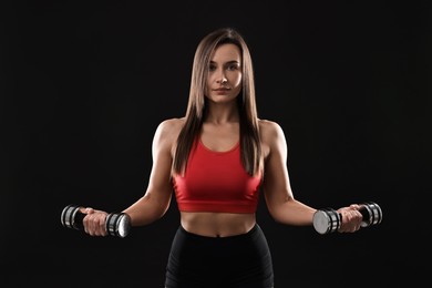 Photo of Woman in gym clothes exercising with dumbbells on black background