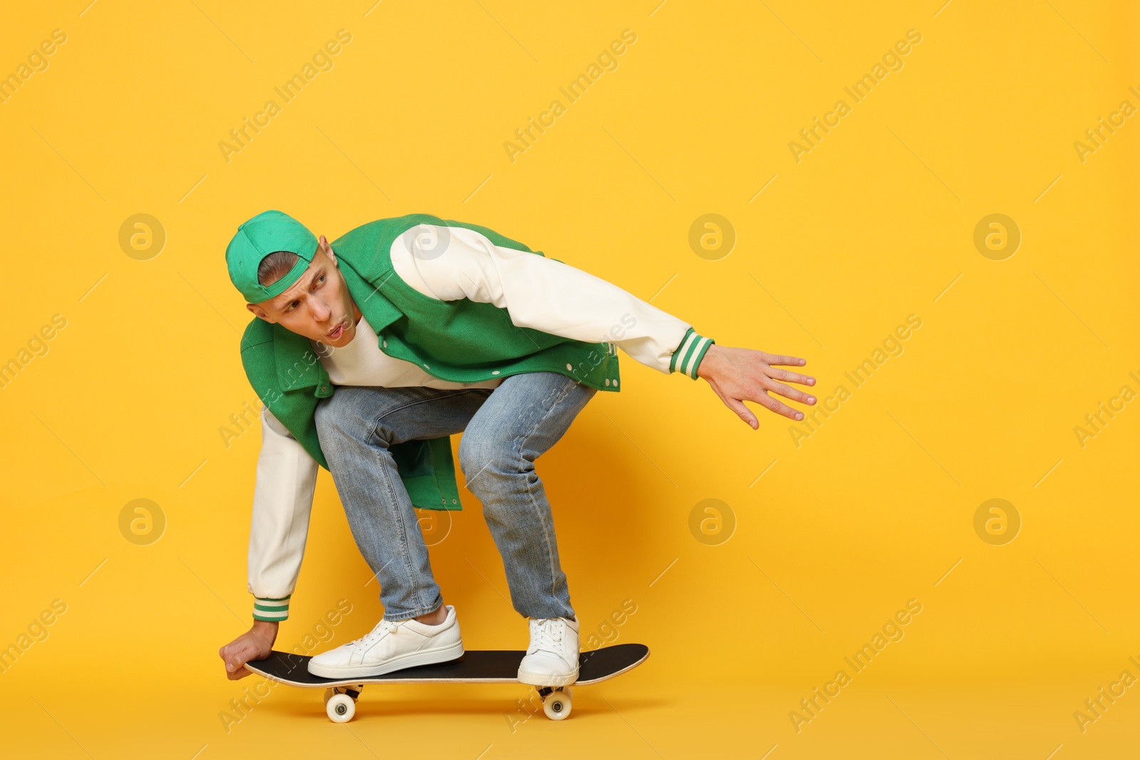 Photo of Handsome man riding skateboard on orange background. Space for text