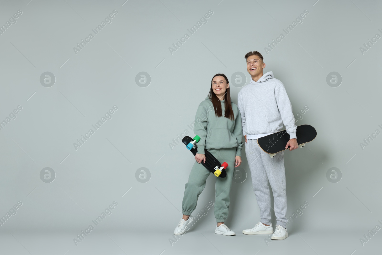 Photo of Happy friends with skateboards on light grey background, low angle view. Space for text