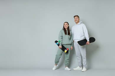 Photo of Happy friends with skateboards on light grey background, low angle view. Space for text