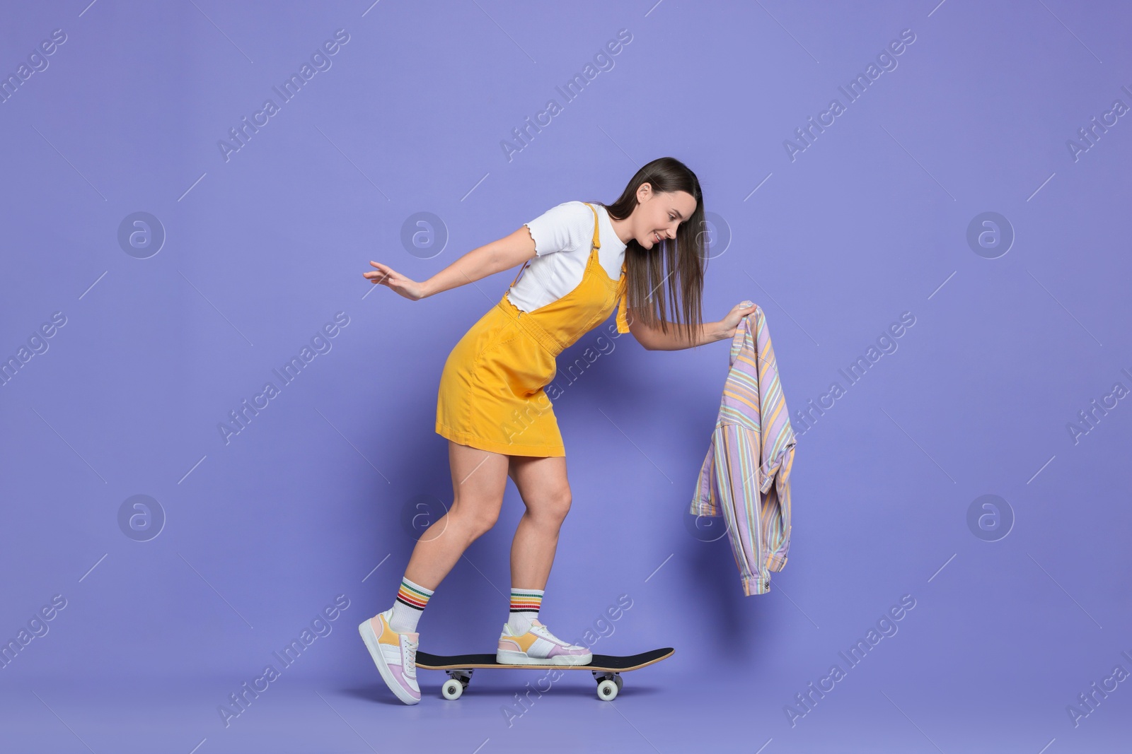 Photo of Smiling woman riding skateboard on violet background