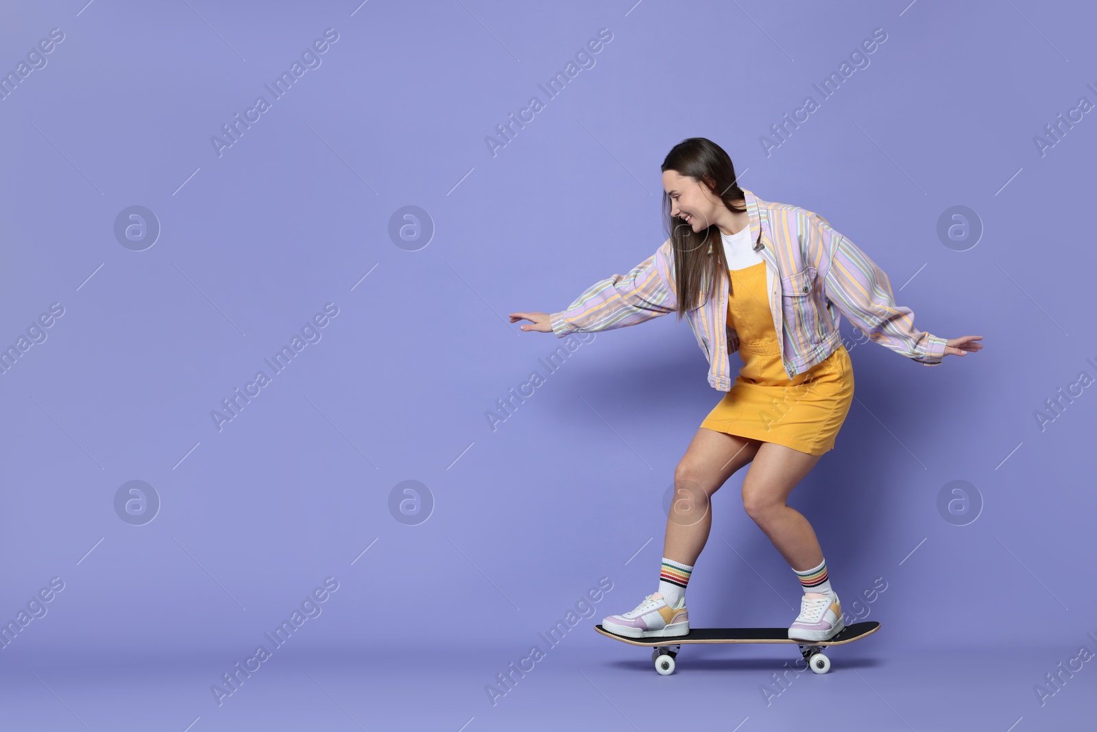 Photo of Smiling woman riding skateboard on violet background. Space for text