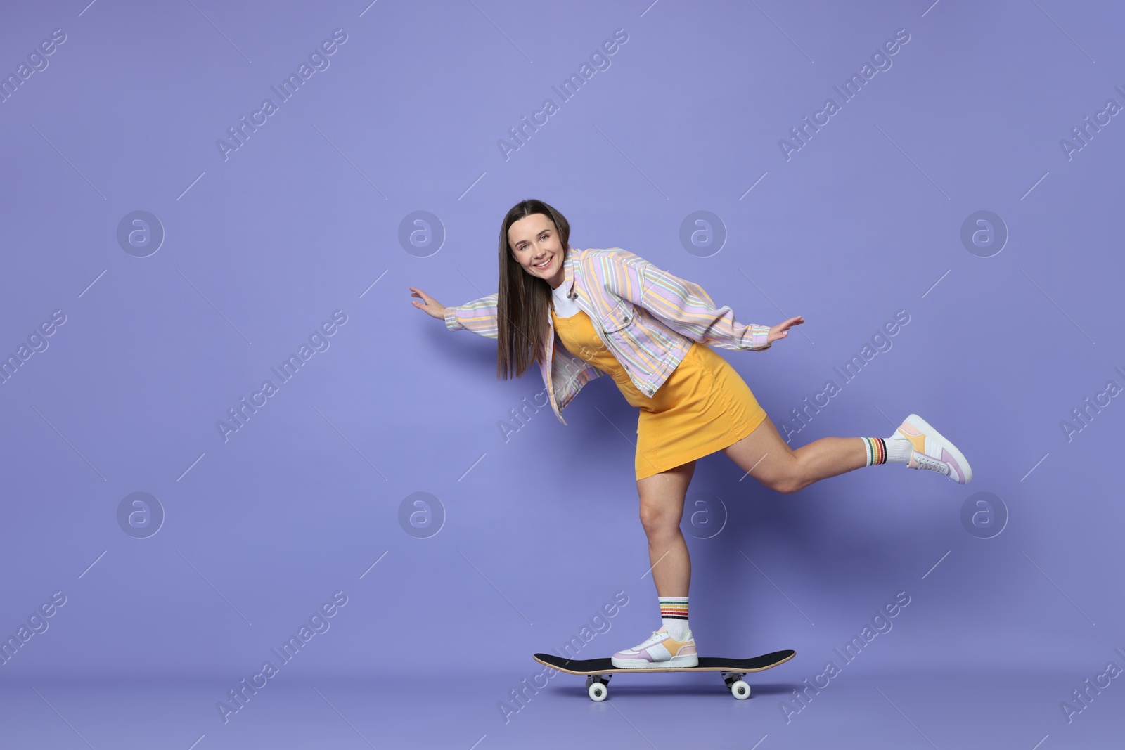 Photo of Smiling woman riding skateboard on violet background. Space for text