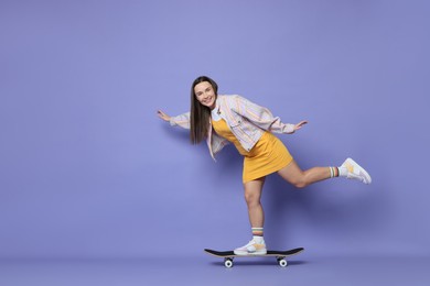 Photo of Smiling woman riding skateboard on violet background. Space for text