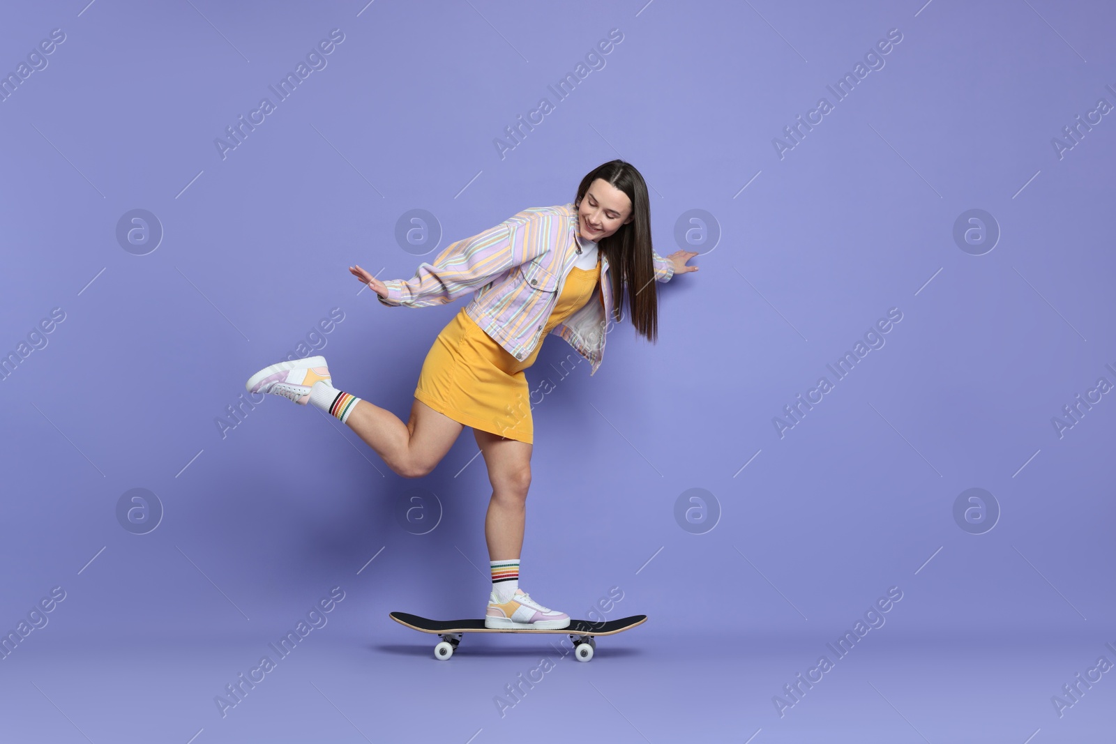 Photo of Smiling woman riding skateboard on violet background. Space for text