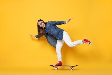 Photo of Smiling woman riding skateboard on orange background