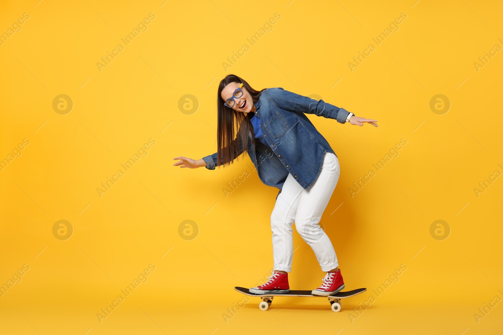 Photo of Smiling woman riding skateboard on orange background. Space for text