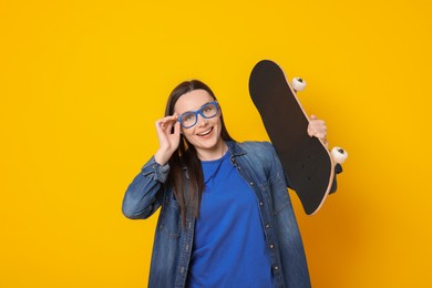 Smiling woman with skateboard on orange background