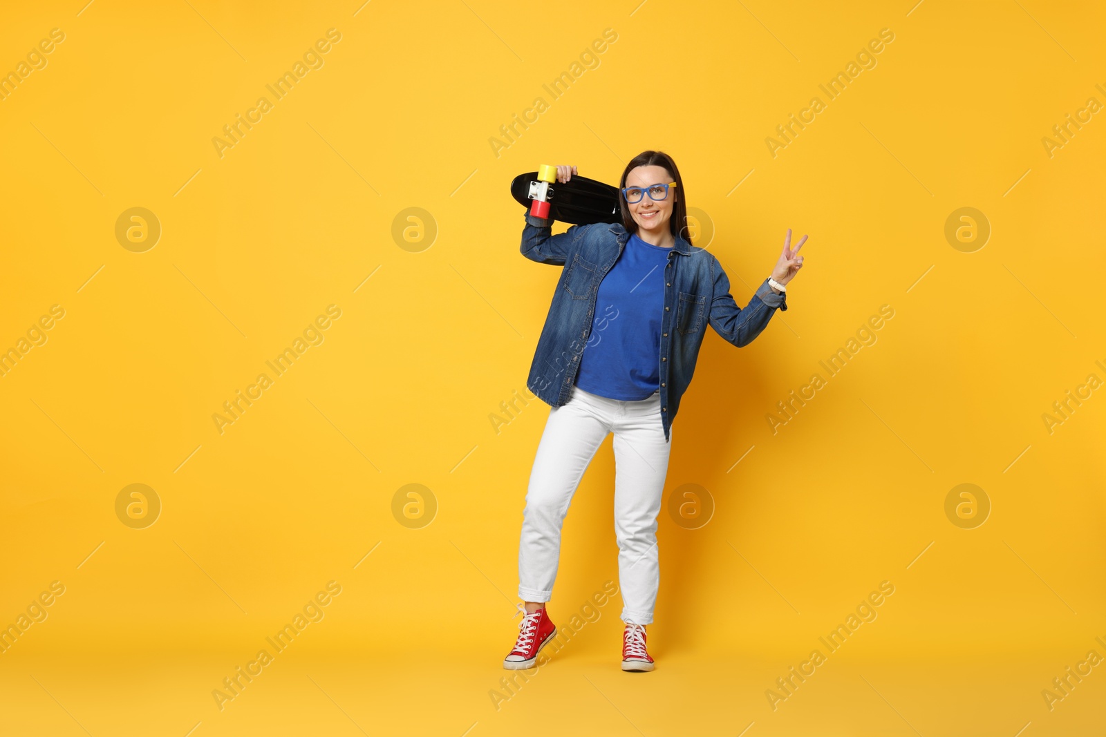 Photo of Smiling woman with penny board showing peace sign on orange background. Space for text