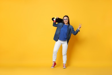 Photo of Smiling woman with penny board showing peace sign on orange background. Space for text