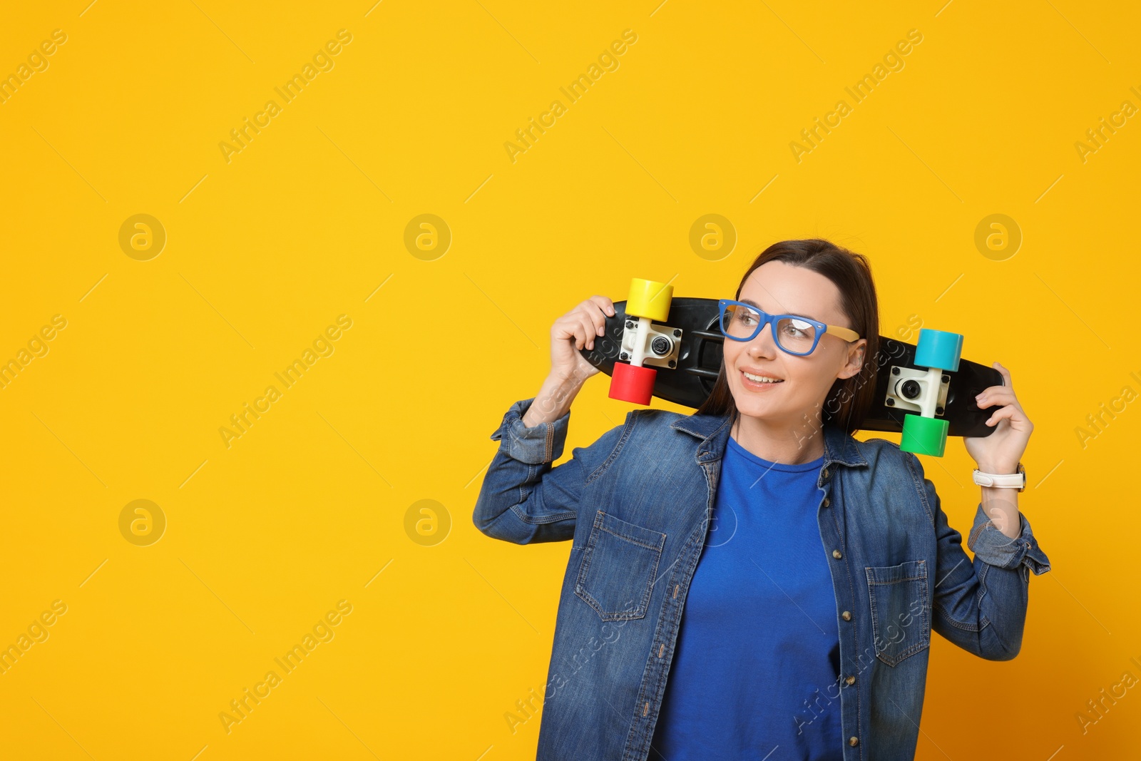 Photo of Smiling woman with penny board on orange background. Space for text