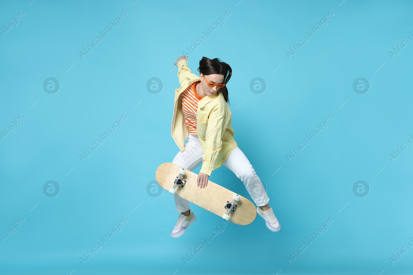 Photo of Beautiful woman jumping with skateboard on light blue background