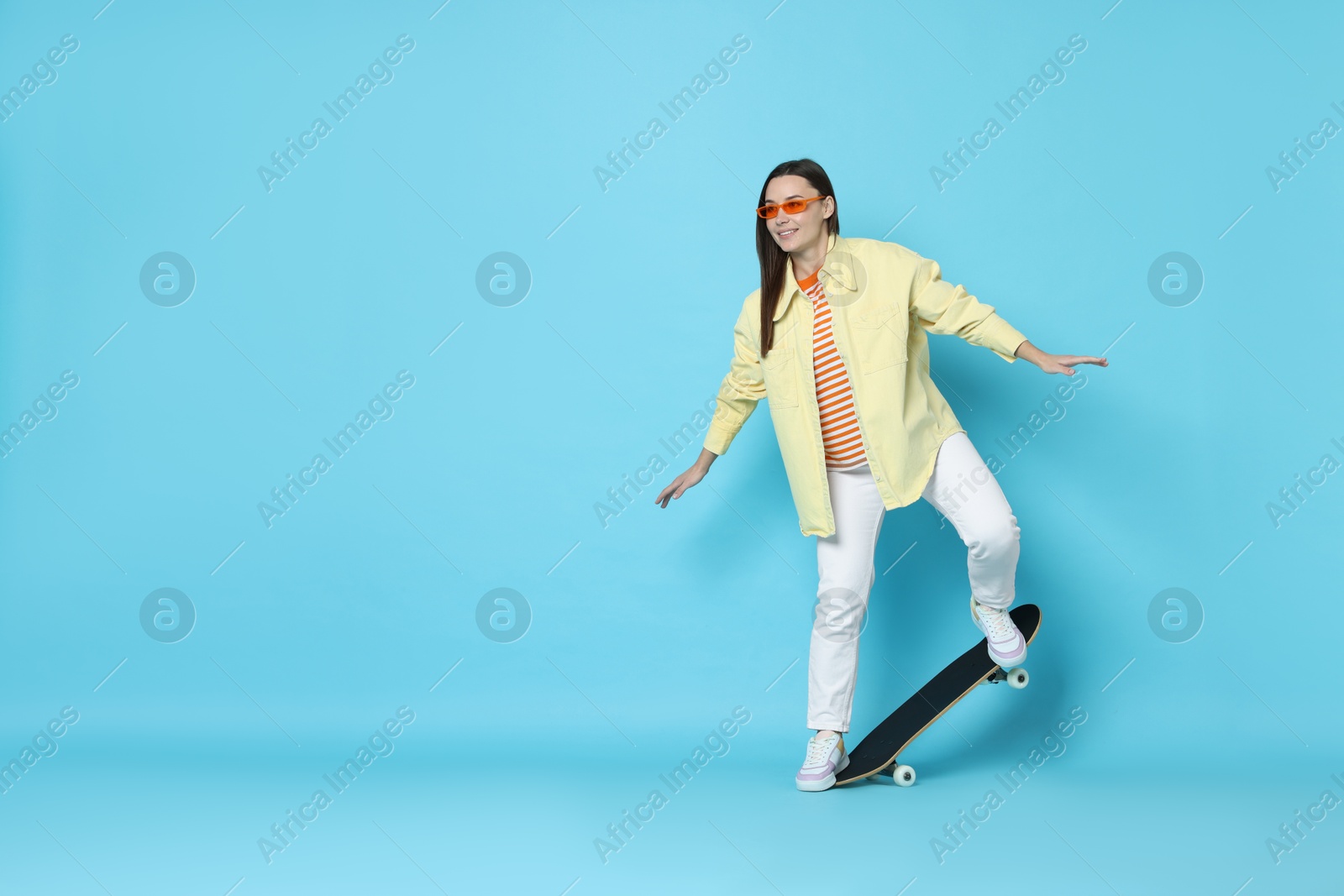 Photo of Smiling woman with skateboard on light blue background. Space for text