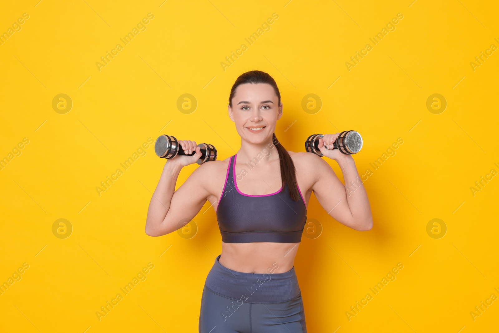 Photo of Smiling woman with dumbbells training on yellow background