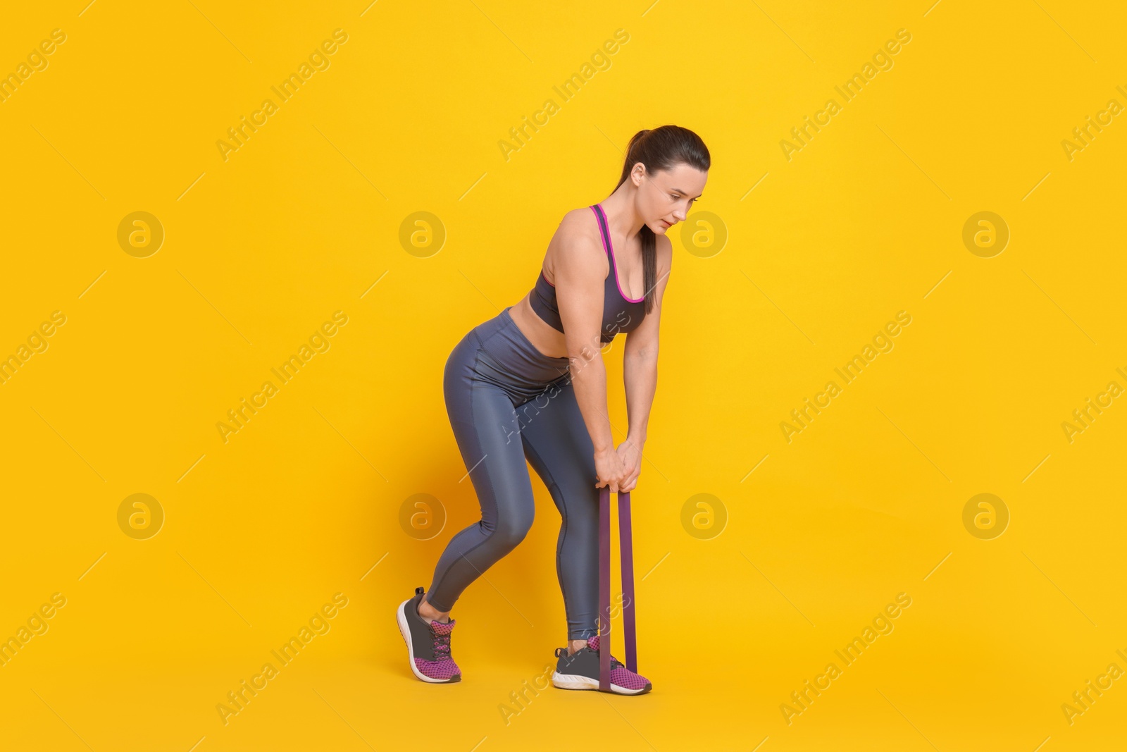 Photo of Beautiful woman with resistance band training on yellow background