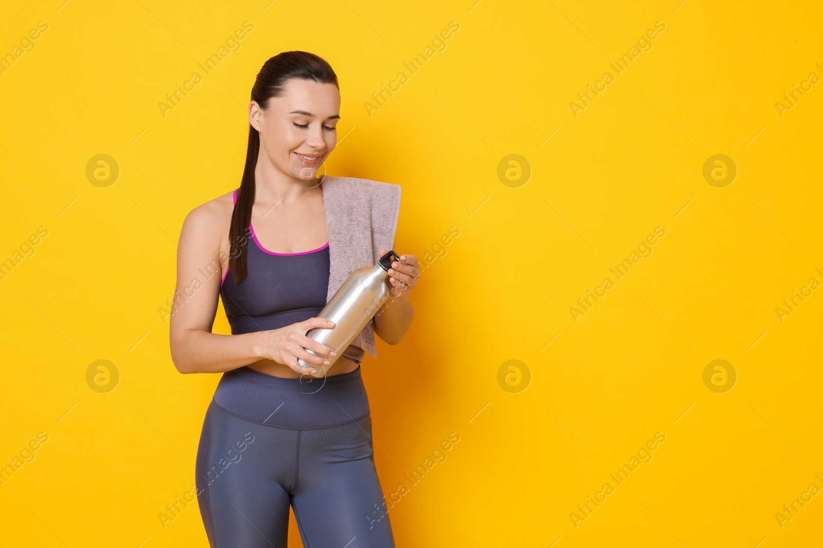 Photo of Smiling woman with thermo bottle and towel on yellow background. Space for text