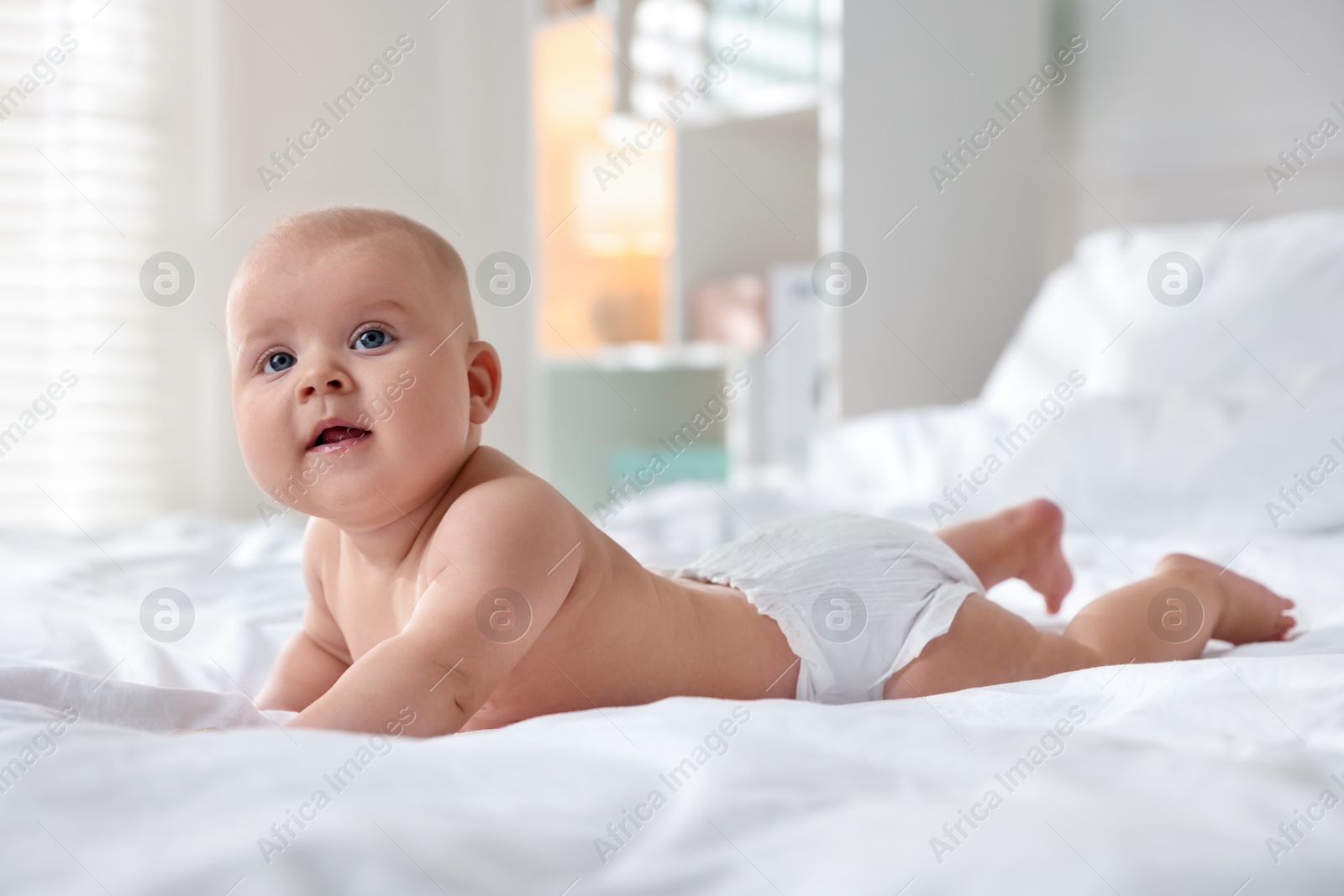 Photo of Cute little baby in diaper on bed indoors