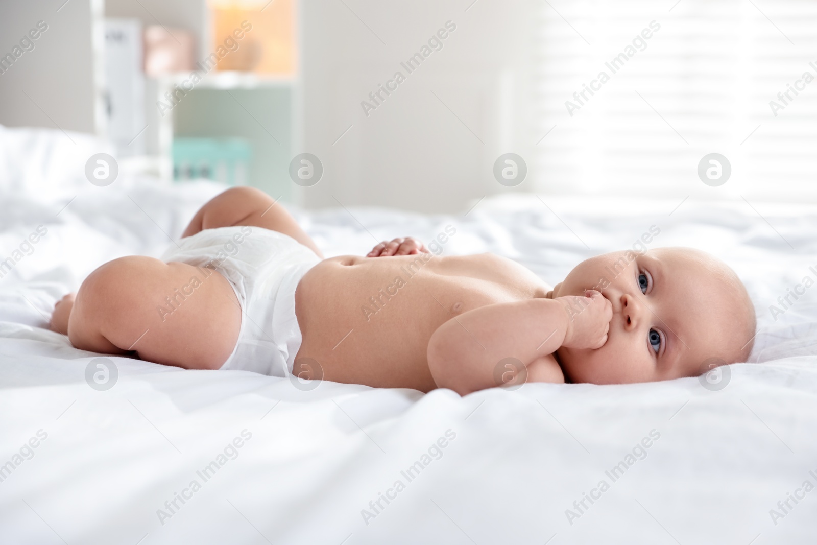 Photo of Cute little baby in diaper on bed indoors