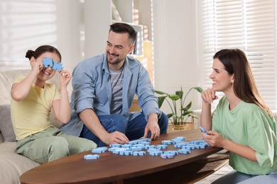 Photo of Happy parents and their daughter solving puzzle together at wooden table indoors