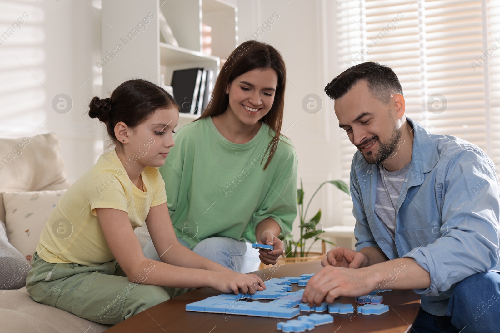 Photo of Happy parents and their daughter solving puzzle together at wooden table indoors