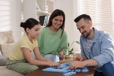 Happy parents and their daughter solving puzzle together at wooden table indoors